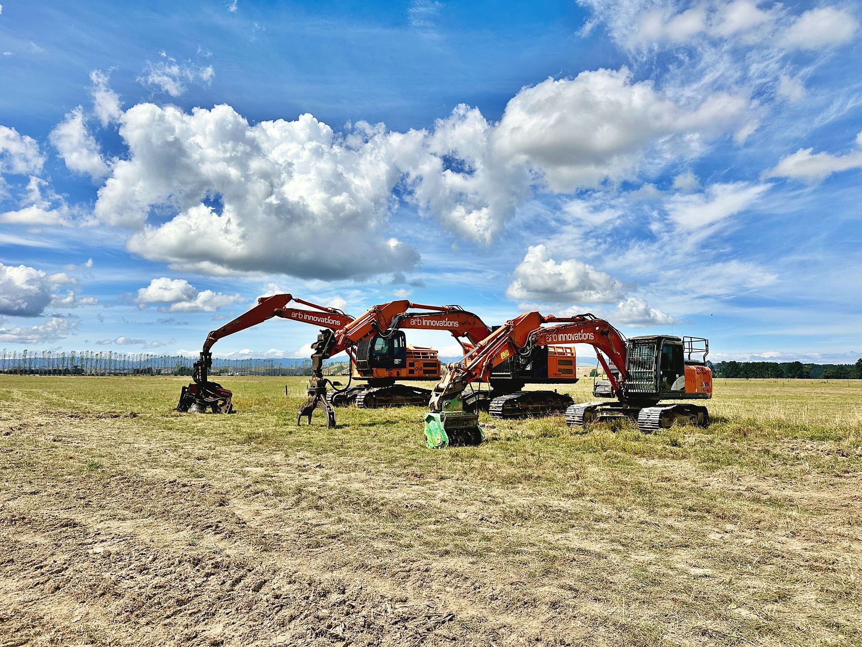 Three Arb Innovations excavators with mulching and grapple attachments lined up on a cleared paddock